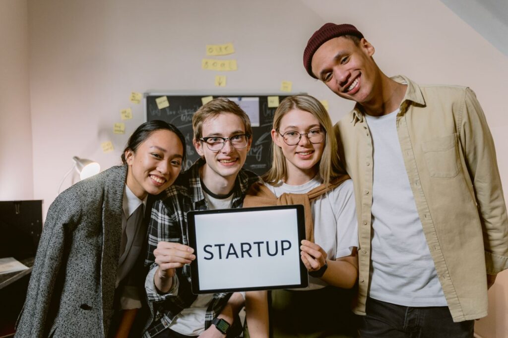 A diverse group of young professionals in a startup office, smiling and holding a sign.